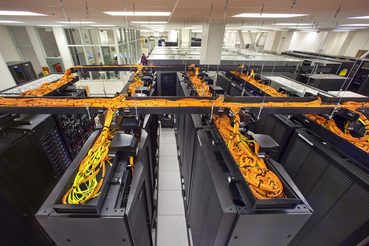 Rows of supercomputer racks with overhead cable trays in a national laboratory data center