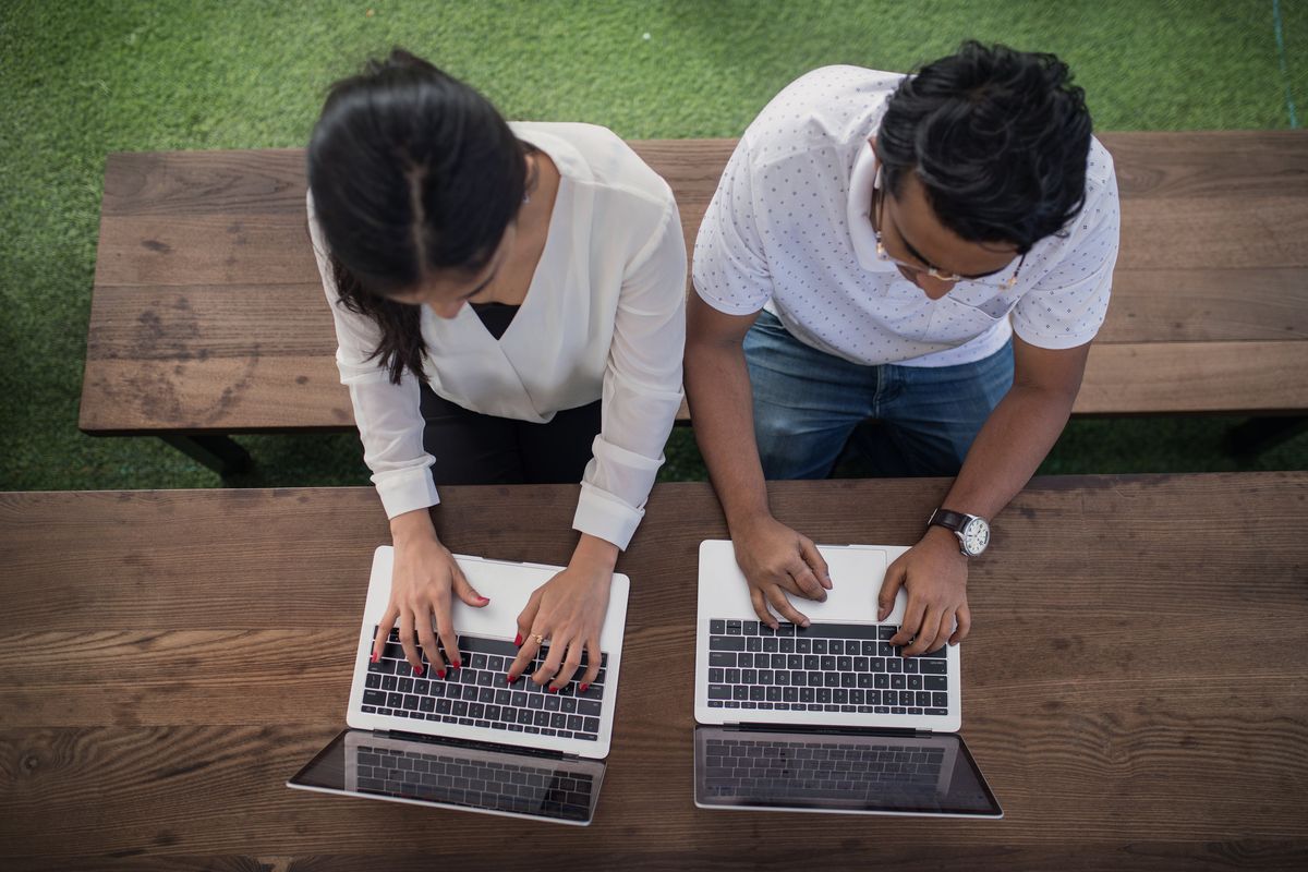 Two colleagues collaborating on laptops at a wooden table